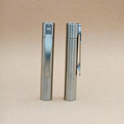 Two ReyLight Pineapple Mini Titanium MK3 - Cylinder pens stand upright on a beige surface; one reveals its clip, while the other highlights a button and small window, showcasing their sleek cylindrical design.