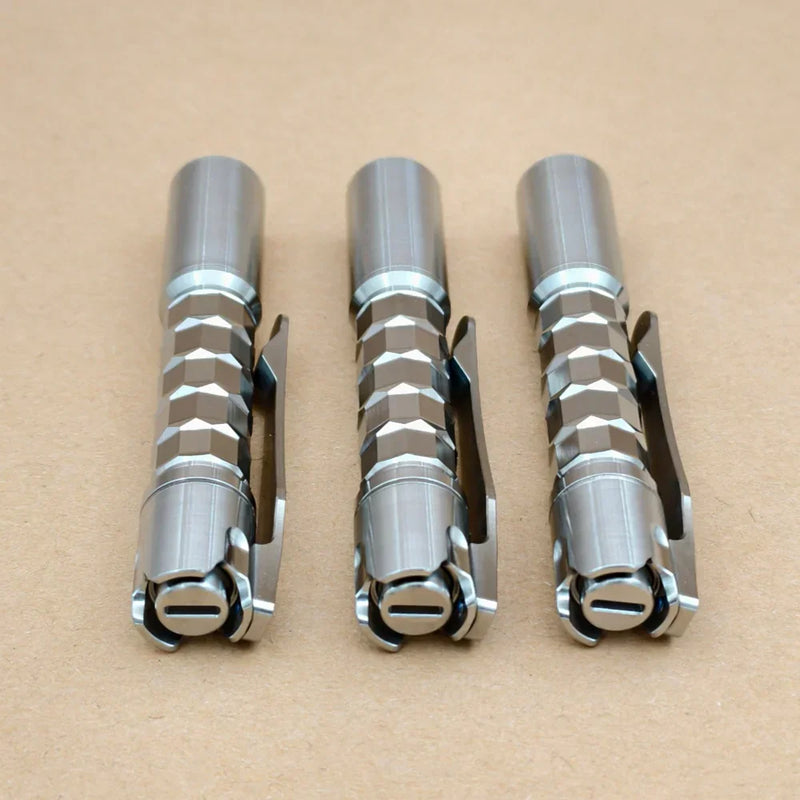 Three ReyLight Pineapple Mini Titanium MK3 - Krystal hexagonal pocket flashlights with clips are arranged side by side on a plain brown surface.