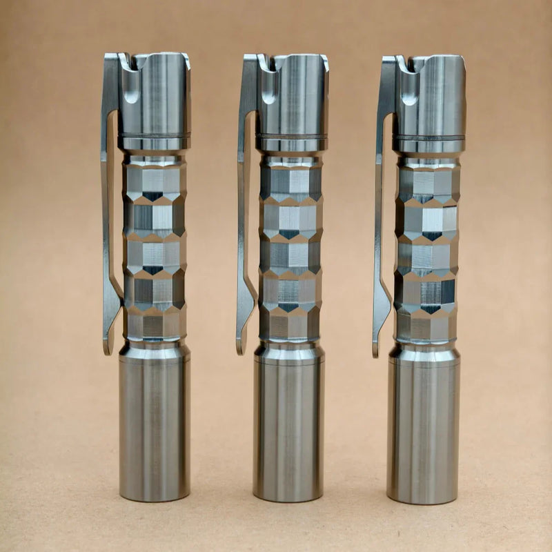 Three ReyLight Pineapple Mini Titanium MK3 - Krystal flashlights stand upright on a light brown surface with a plain background, showcasing their hexagonal grip patterns.