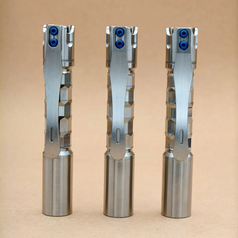 Three ReyLight Pineapple Mini Titanium MK3 - Krystal flashlights with hexagonal-patterned grips and pocket clips stand upright on a plain tan surface.