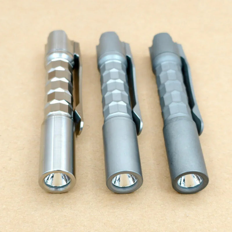 Three ReyLight Pineapple Mini Titanium MK3 - Krystal flashlights with hexagonal grips and clips are arranged side by side on a plain brown surface.