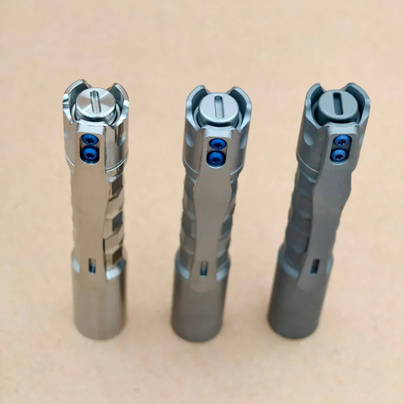 Three ReyLight Pineapple Mini Titanium MK3 - Krystal flashlights with blue screws and textured grips stand upright side by side on a plain beige surface.