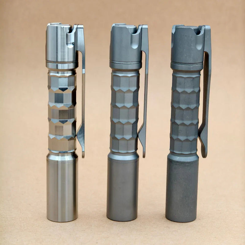 Three ReyLight Pineapple Mini Titanium MK3 - Krystal flashlights with textured grips and pocket clips stand upright on a plain brown surface.