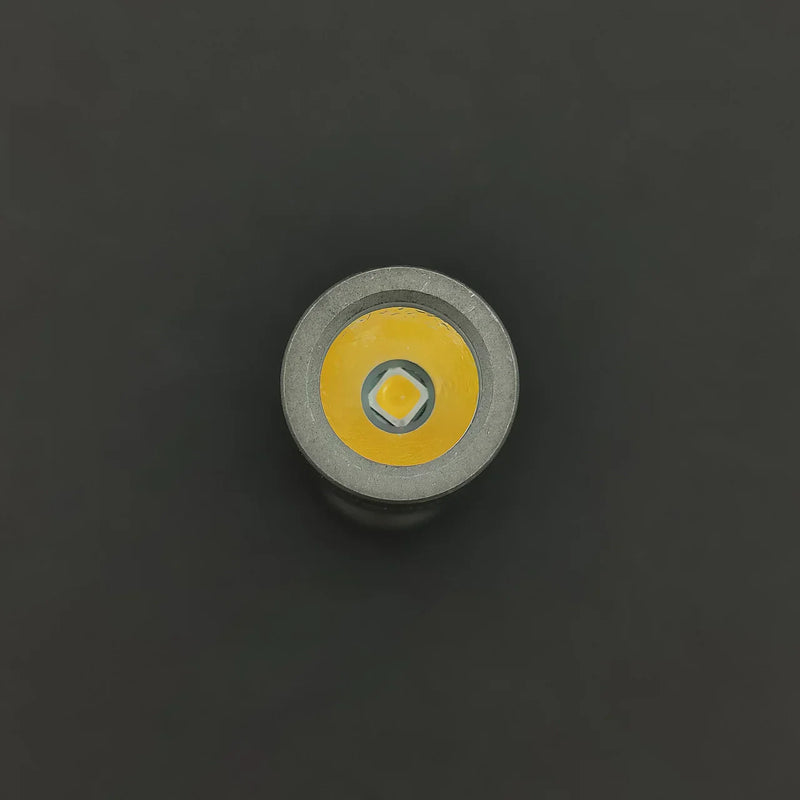 A close-up top view of the ReyLight Pineapple Mini Titanium - MK3 flashlight head shows a yellow circular reflector and a small high-CRI LED diode in the center against a dark background.