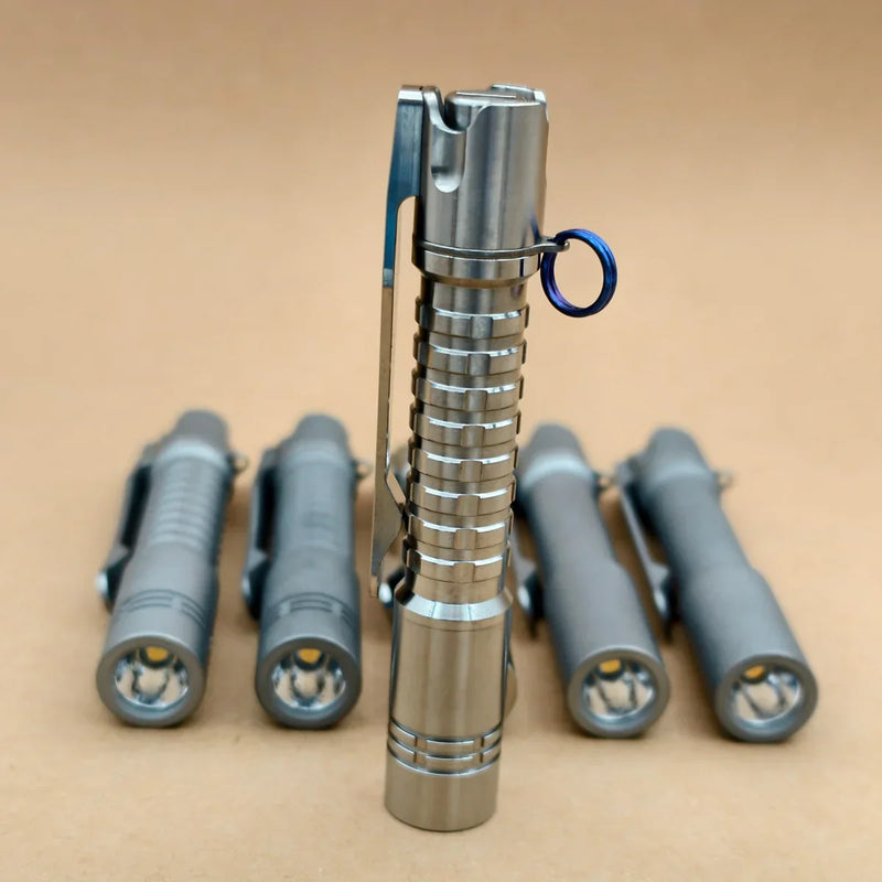 Five metal flashlights, including the ReyLight Pineapple Mini Titanium - MK3 perfect for everyday carry, are displayed on a tan surface—one stands upright in front with four lying down in the background.