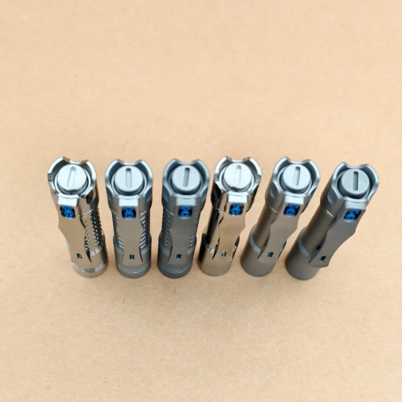 Six metallic flashlights, including the ReyLight Pineapple Mini Titanium - MK3 with a high-CRI LED, stand upright in a row on a light brown surface—perfect for your everyday carry collection.