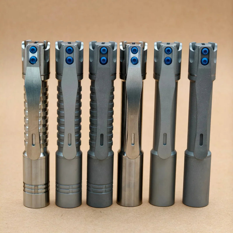 Six ReyLight Pineapple Mini Titanium - MK3 bolt-action pens with blue screws stand upright in a row against a plain brown background, perfect for everyday carry.