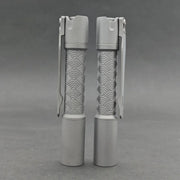 Two ReyLight Pineapple Mini Titanium - MK3 cylindrical flashlights with wave-patterned grips stand upright on a gray surface—stylish and reliable EDC options for any occasion.