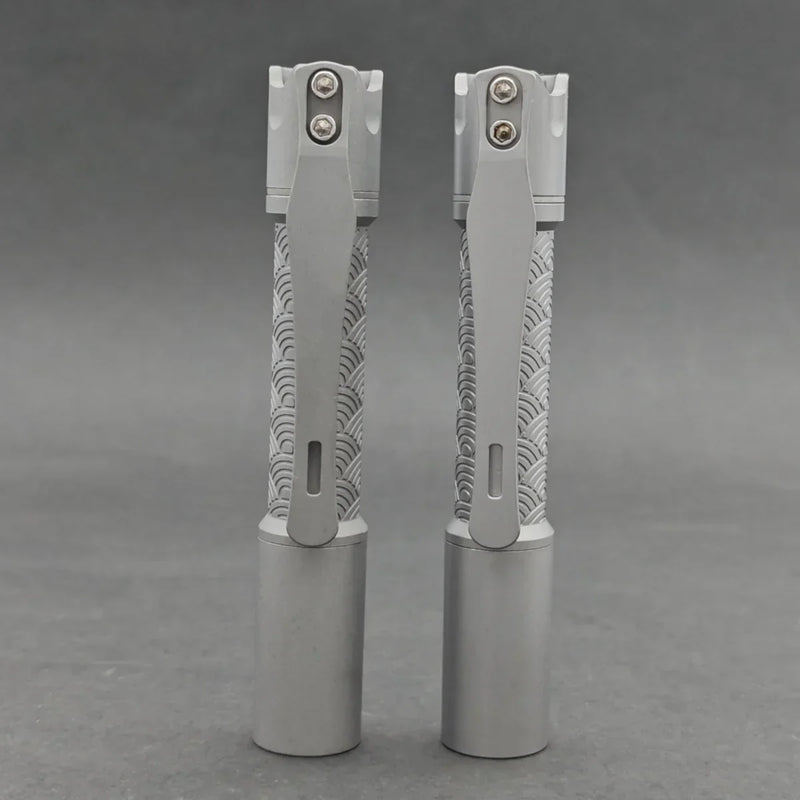Two ReyLight Pineapple Mini Titanium - MK3 EDC flashlights with patterned grips stand upright on a gray surface against a gray background.