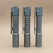 Three ReyLight Pineapple Mini Titanium - MK3 flashlights in gray, each with a pocket clip and unique grip texture, stand upright side by side on a plain light brown surface, showcasing their EDC-friendly design.