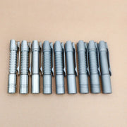 Nine metallic pens with varied textured grips line up on a light brown surface—perfect for your everyday carry, along with essentials like the ReyLight Pineapple Mini Titanium - MK3 flashlight.