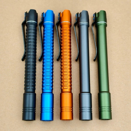 Five metal pen-shaped flashlights, including a rechargeable penlight and the ReyLight Pineapple Penlight-MK II Aluminum with high-CRI LED, are arranged vertically in black, blue, orange, gray, and green on a tan surface—each with a side clip.