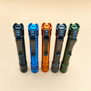 Five metal pens in black, blue, orange, dark gray, and green stand upright on a beige surface—each showcasing the sleek style of the ReyLight Pineapple Penlight-MK II-Aluminum.