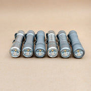 Six metal EDC flashlights, including the ReyLight Pineapple Titanium, are arranged side by side on a plain beige surface with their lenses facing forward.