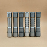 Six metallic EDC flashlights with different textured grips, including the ReyLight Pineapple Titanium, stand upright in a row against a plain beige background.