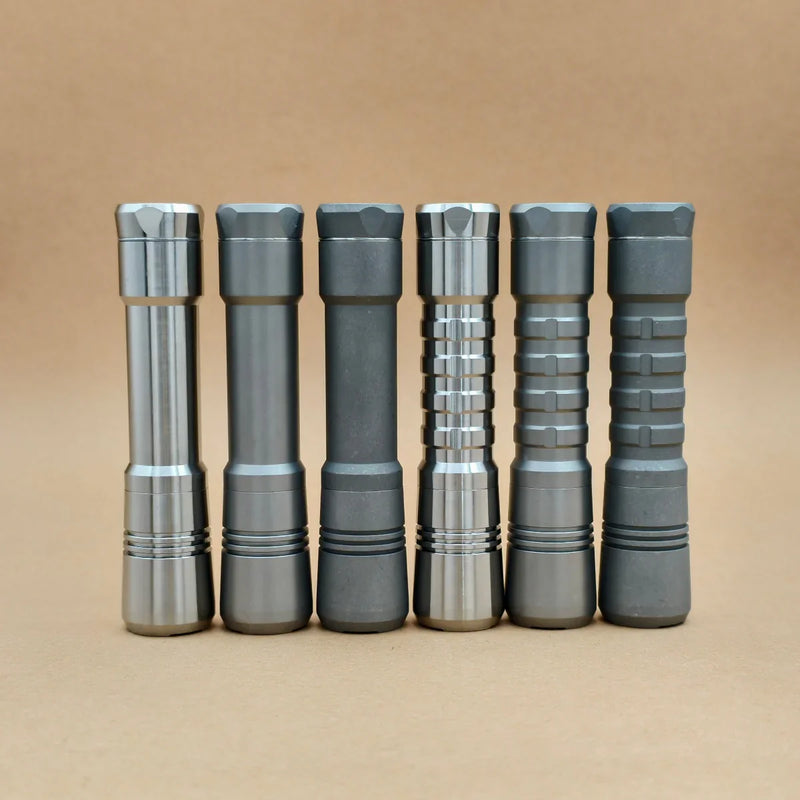 Six metallic EDC flashlights with different textured grips, including the ReyLight Pineapple Titanium, stand upright in a row against a plain beige background.