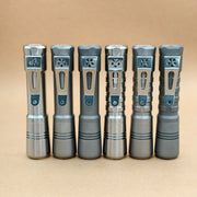 Six metallic EDC flashlights with varied grips and designs, including the ReyLight Pineapple Titanium, are displayed upright in a row against a plain brown background.