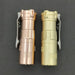 Two small flashlights, one copper and one brass, gleam side by side against a dark backdrop. Each ReyLight Rook features the Nichia 519a LED and a convenient, stylish clip on its side.