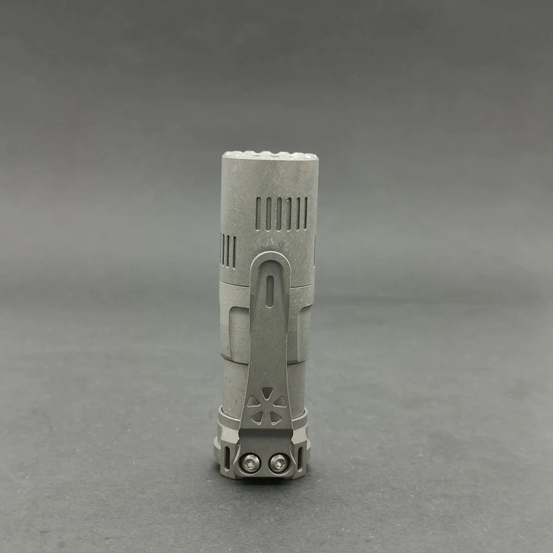 The ReyLight Rook - Ti is a compact metallic flashlight with a clip, featuring a Nichia 519a LED, displayed against a plain gray background.