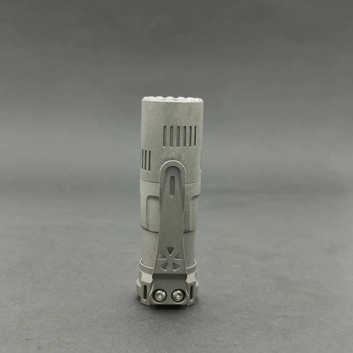 A small silver Reylight Rook - Ti flashlight sitting on a gray surface.