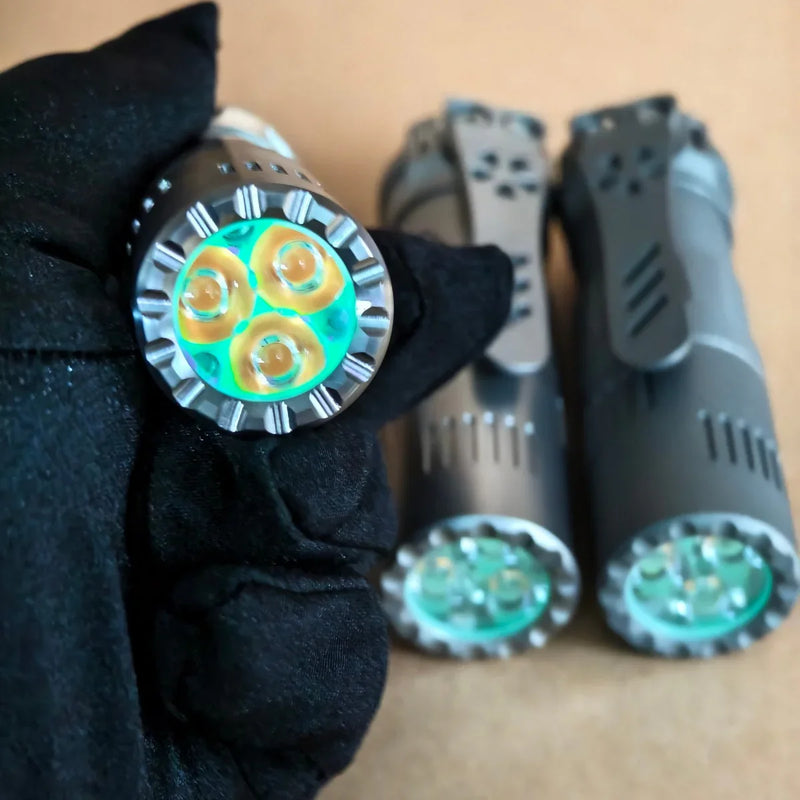 A gloved hand holds a compact ReyLight Rook - Ti flashlight with three LEDs; two similar 18350 battery-compatible flashlights and visible LEDs are on a tan background.