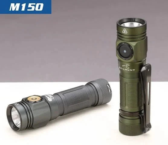 Two compact LED flashlights, including a black EDC and a green Skilhunt M150 V4 AA 14500 USB with clip, are shown on a light surface; the green Skilhunt stands upright and the black flashlight lies horizontally.