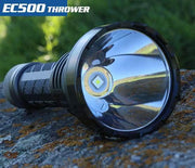A Skilhunt EC500 USB-C rechargeable flashlight with a reflective lens sits on a rock. Text reads "EC500 Thrower," featuring 2100 lumens for an exceptional long-range flashlight experience.