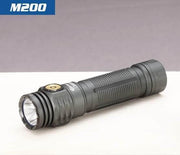 A compact black Skilhunt M200 V4 flashlight with magnetic charging rests on a light surface against a gray background.