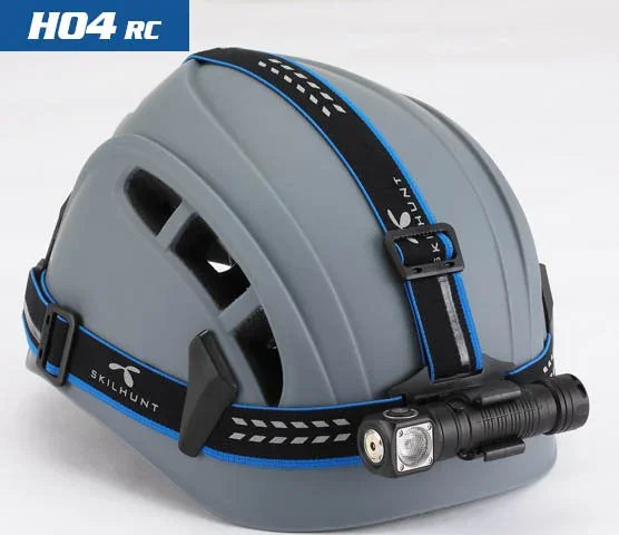 A grey safety helmet with black and blue straps, featuring a Skilhunt H04 RC / H04R RC USB Rechargeable Headlamp mounted on the front.