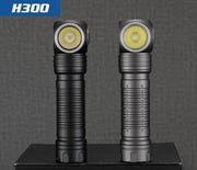 The Skilhunt H300/H300R Headlamp, available in black and gray, features a right-angle design with CREE XHP50.3 LEDs. Shown upright on a black surface under a blue "Skilhunt H300" label, it's ideal as an LED headlamp or handheld light.