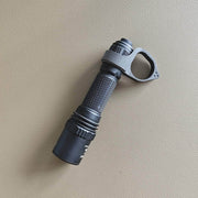 A black tactical flashlight featuring a textured grip and a Weltool FR20 tactical ring attachment rests on a light brown, textured surface.
