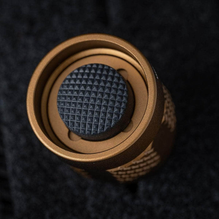 A close up of a gold and black button on a black surface featuring the Weltool TC68/TC68N Tailcap for W35/W65.