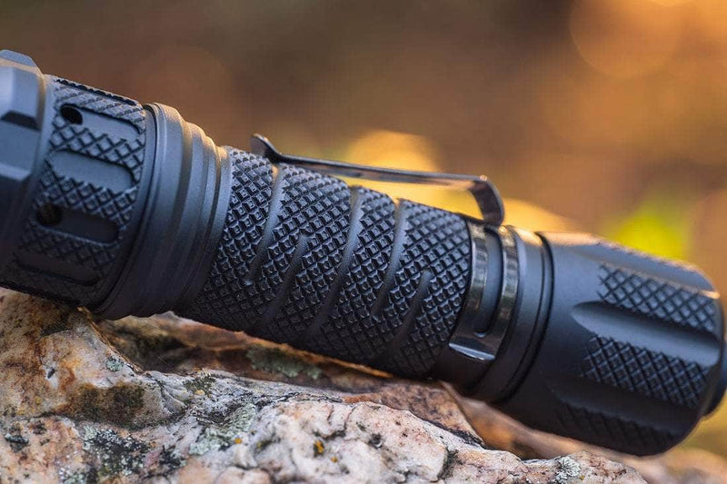 Close-up of a Weltool BB50 body with TC81 tail cover, black and textured, resting on a rock against a blurred, warm-toned background.