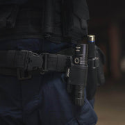 A close-up of a person in dark tactical gear and a utility belt holding the Weltool F8R rechargeable LED flashlight with USB-C charging, along with other essential tools.
