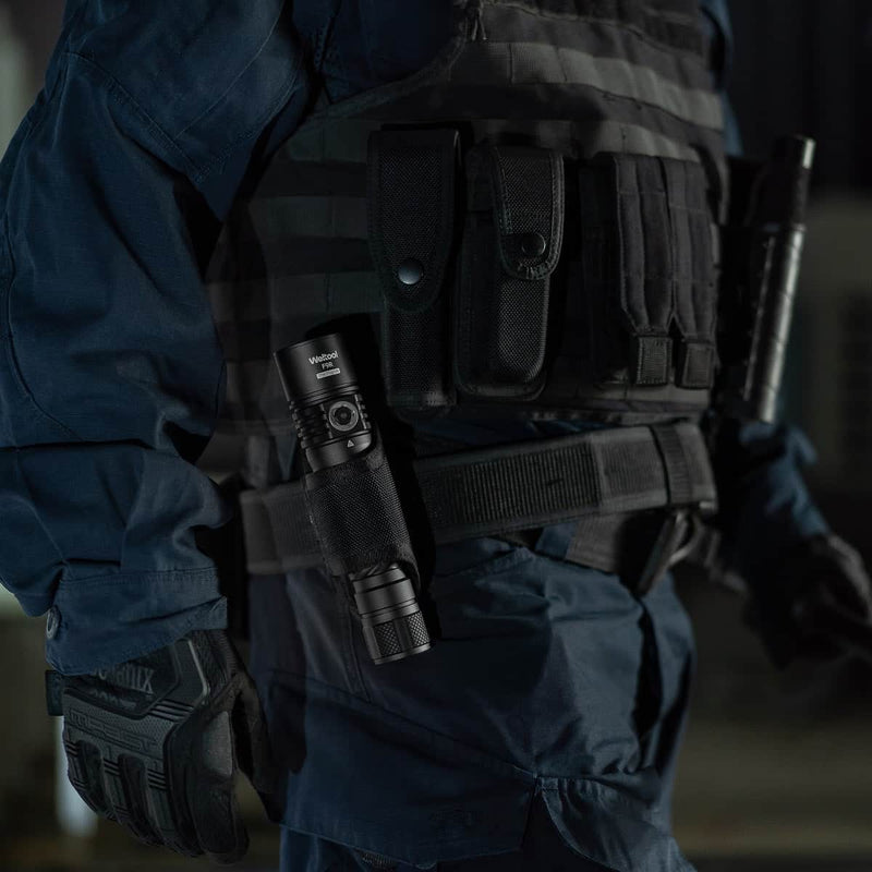 A person in tactical gear with a Weltool F9R high lumen rechargeable LED flashlight attached to their belt, wearing gloves and a vest with multiple pouches.