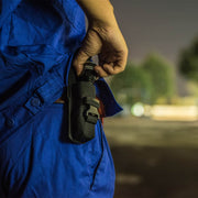 Outdoors at night, a person in blue clothing tucks a flashlight into a Weltool FH1 FH2 V2.0 CORDURA Flashlight Holster worn on their waist.