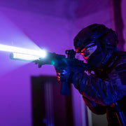Wearing tactical gear and a helmet, a person aims a rifle fitted with the Weltool LH20, its 700-lumen LEP beam and aluminum reflector slicing through the dark, blue- and purple-lit indoor environment.
