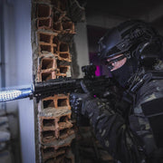 A tactical officer in black gear aims a rifle equipped with the Weltool LH20 LEP weapon light, delivering 700 lumens with an aluminum reflector, through a damaged brick wall inside a building.