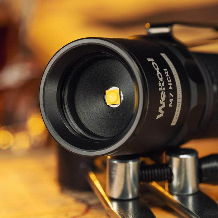 Close-up of the Weltool M7 High-CRI flashlight head featuring a 4000K LED bulb, with part of the flashlight body and a clamp visible in the foreground.