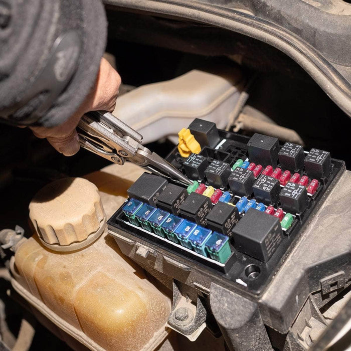 A person uses pliers to remove a fuse from a car fuse box under the hood, illuminated by the Weltool M7 High-CRI flashlight with a 4000K color temperature.