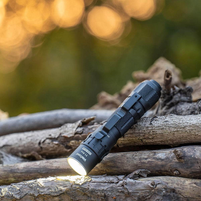 A Weltool T1 Pro TAC turned on, resting on a pile of weathered logs, with a blurred background of warm golden light.