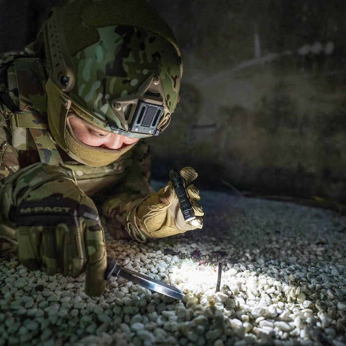 Sentence with replaced product name: A soldier in camouflage examining an object on the ground with a Surefire G2X Pro dual-output LED flashlight at night.