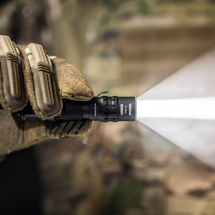 Sentence with Product Name: A close-up of a hand in a camouflage military uniform holding a black Olight M2R Pro Warrior tactical flashlight emitting a bright beam of light.