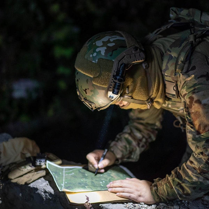 A soldier in camouflage gear using a Weltool T1 Pro TAC flashlight to read a map at night.