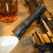 A Weltool T12 flashlight with high lumens, placed next to a gun and a glass of whiskey.