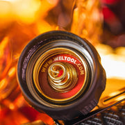 A Weltool T12 with a gold lid emitting lumens as it sits on top of a fire.