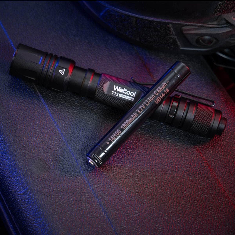 Two black Weltool T15 LED tactical flashlights rest on a textured dark surface, illuminated by blue and red light.
