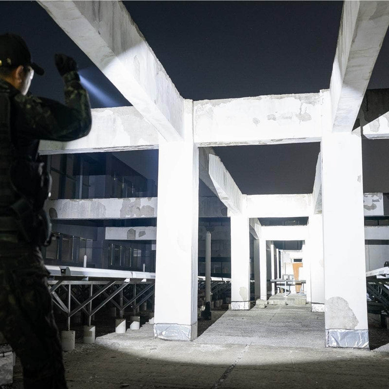 A person wearing dark clothing uses the rechargeable Weltool T15 flashlight to scan an empty, unfinished concrete structure at night.
