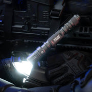 A lit Weltool T15 LED tactical flashlight sits atop tactical gear, with black gloves and equipment visible in the background.
