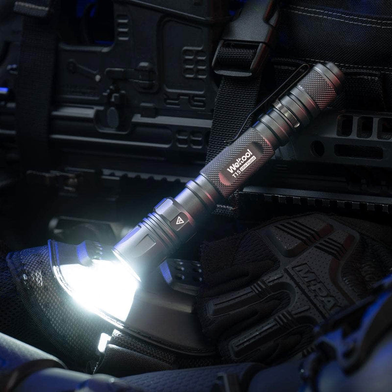 A lit Weltool T15 LED tactical flashlight sits atop tactical gear, with black gloves and equipment visible in the background.